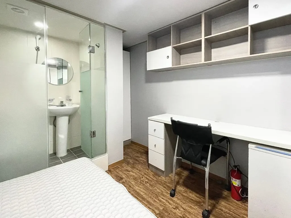 A clean, compact Goshiwon room featuring a small desk, single bed, and private bathroom, illustrating low-cost, no-deposit housing for students in Seoul.